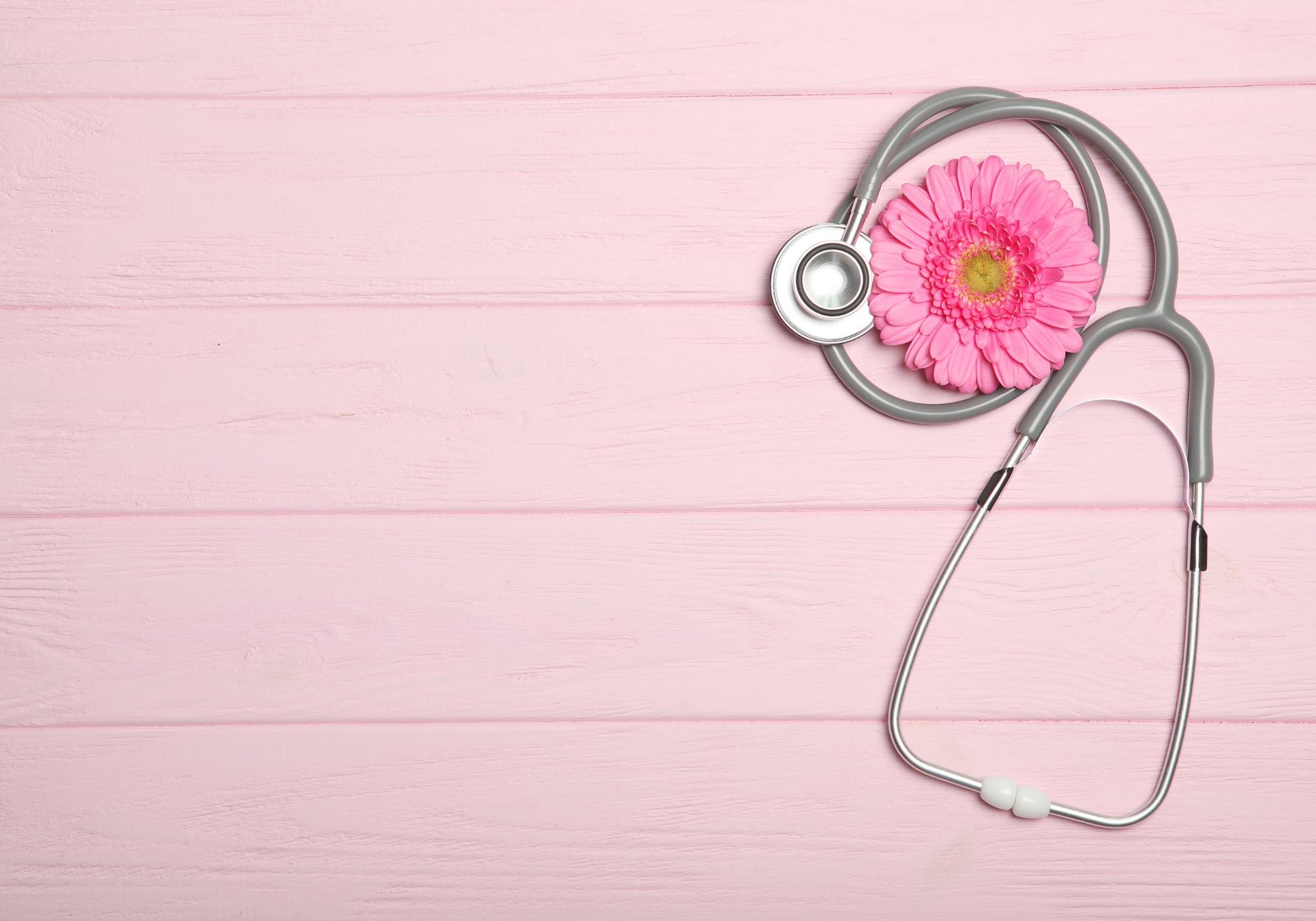 Stethoscope with a pink flower on a pink wooden background